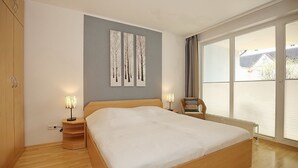 Een slaapkamer met een groot bed, een houten garderobe, bedlampjes en uitzicht door een groot raam.