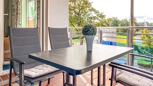 Un balcon avec une table et des chaises, un pot de fleurs et une vue sur un parc.