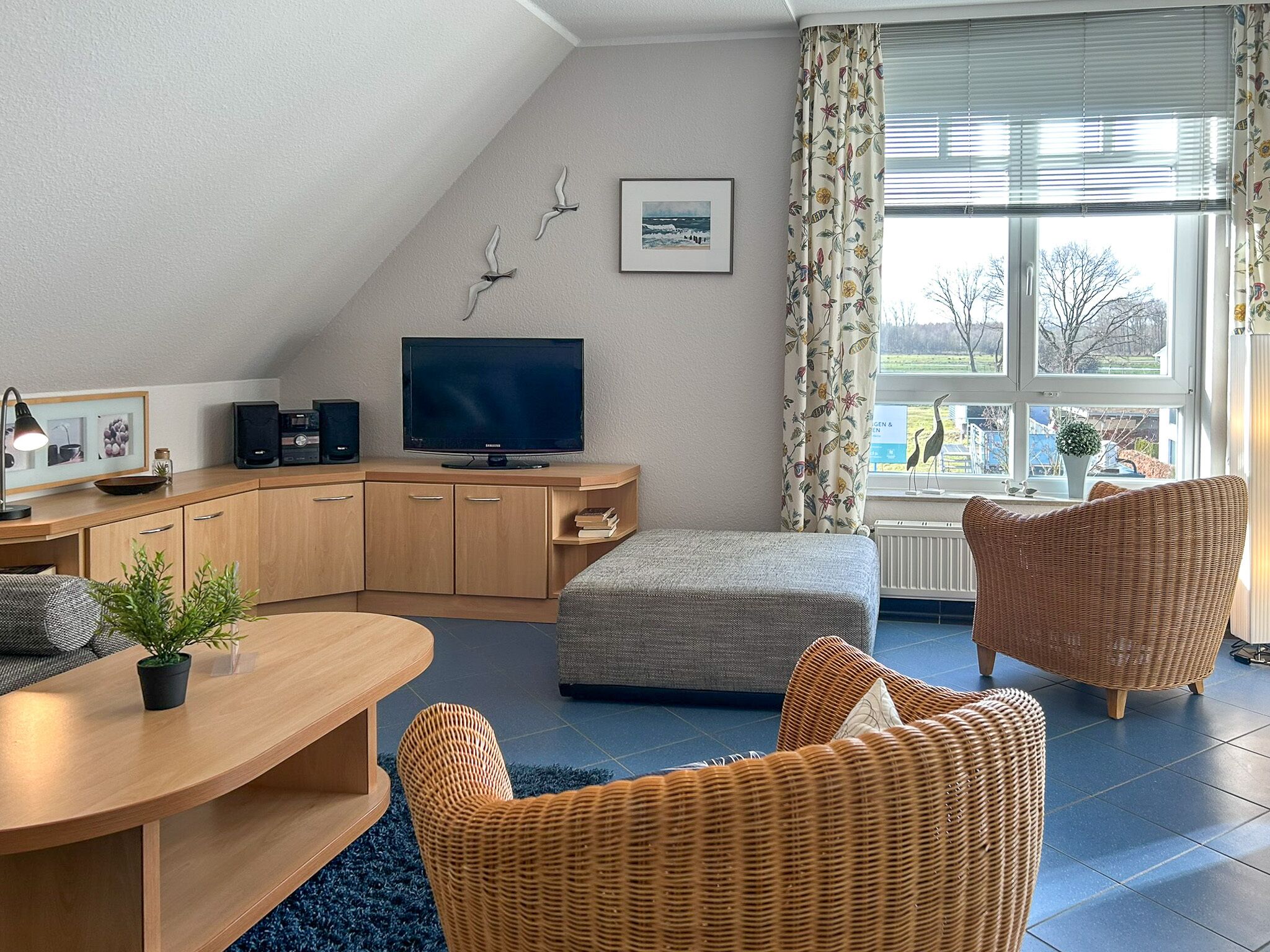 Ein modernes Wohnzimmer mit einem gewölbten Holztisch, Korbstühlen, einem Fernseher und einem Fenster mit Vorhängen.