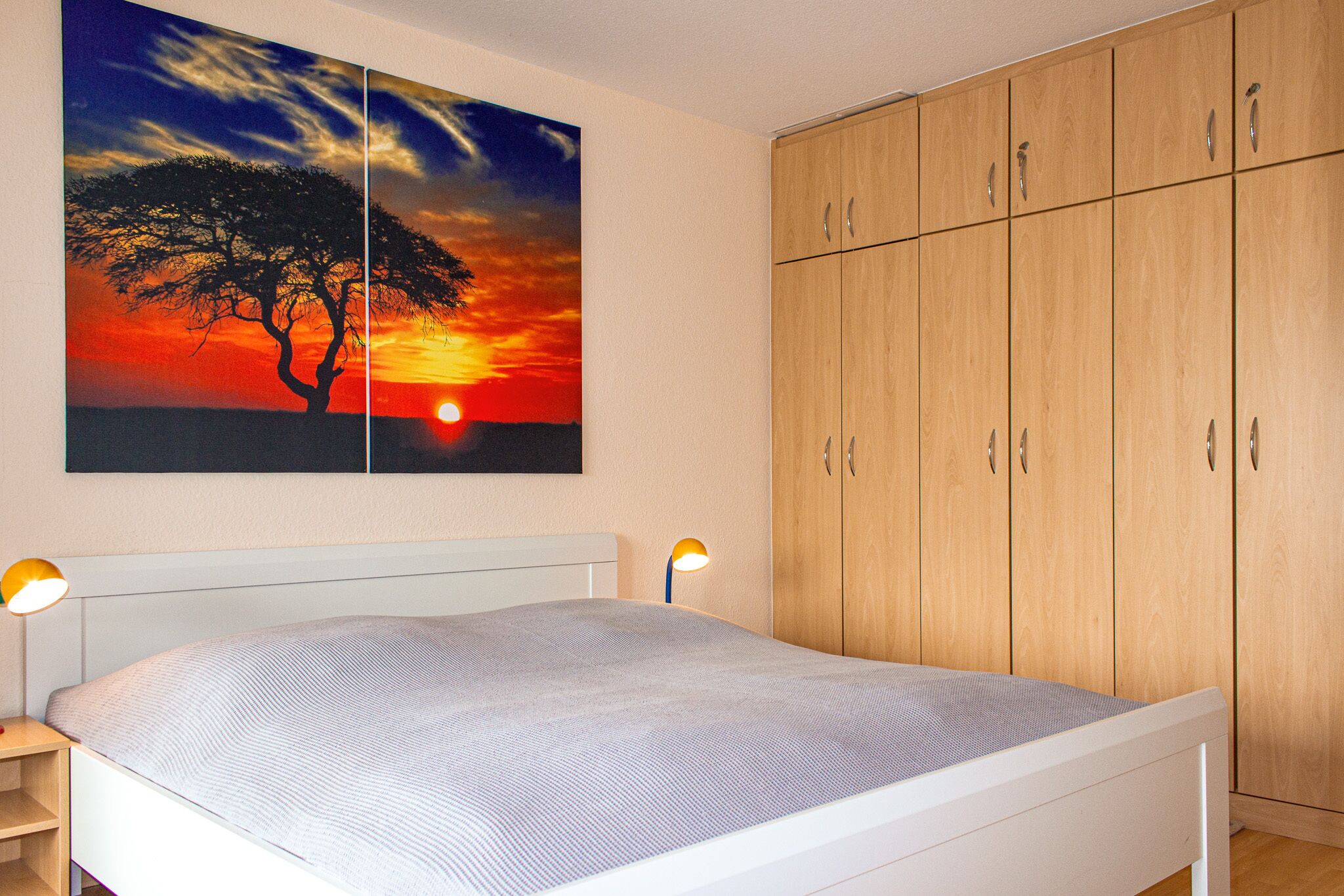 A bedroom with a bed, nightstands, a wall-mounted lamp, and a large wooden wardrobe.