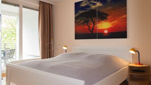 Une chambre à coucher avec un lit, deux lampes de chevet, une fenêtre avec des rideaux et un tableau représentant un coucher de soleil accroché au mur.