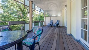 A covered outdoor area with a wooden deck, a round table, and two chairs with colorful upholstery. - Likedeeler II Wohnung 2 (Ostseebad Boltenhagen)