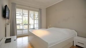 A bedroom with a large bed, a TV mounted on the wall, a bedside table, and a window with curtains. - Likedeeler II Wohnung 2 (Ostseebad Boltenhagen)
