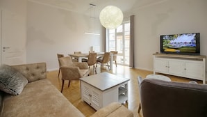 A modern living room with a sofa, chairs, a coffee table, a TV, and a dining area with a table and chairs. - Likedeeler II Wohnung 2 (Ostseebad Boltenhagen)