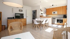 Una cocina moderna con armarios de madera, microondas y estufa. Hay una zona de comedor con una mesa y sillas blancas.