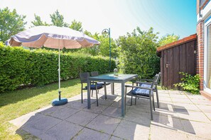 Un patio al aire libre con una mesa, sillas, una sombrilla y un seto de fondo.