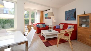 Una sala de estar moderna con una mesa blanca, sofás rojos, sillas de mimbre y un aparador con vajilla.