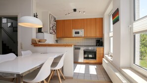 Una cocina moderna con armarios de madera, una encimera blanca y un comedor con mesa y sillas blancas.