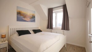 Un dormitorio con cama, una mesita de noche, una ventana con cortinas y un cuadro en la pared.