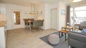 Una sala de estar moderna con un sofá gris, una mesa de comedor de madera con sillas y una pequeña mesita auxiliar de madera.
