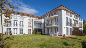 Un immeuble résidentiel à plusieurs étages, doté de balcons, d’une pelouse bien entretenue et d’un espace extérieur aménagé pour s’asseoir.