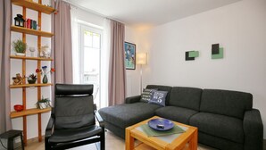 Un salon avec un canapé gris, un fauteuil noir, une table basse en bois et une bibliothèque contenant divers objets décoratifs.