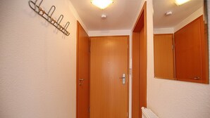 Un couloir étroit avec une porte en bois, un radiateur et un miroir accroché au mur.
