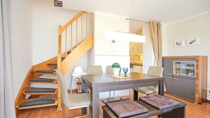 Ein modernes Interieur mit einer Holztreppe, einem Esstisch mit gepolsterten Bänken, einer Küchenzeile und einem Schrank mit Gläsern.