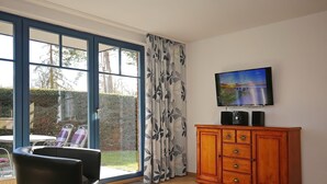 Ein Zimmer mit großem Fenster, Fernseher, Holzschrank und Stuhl.