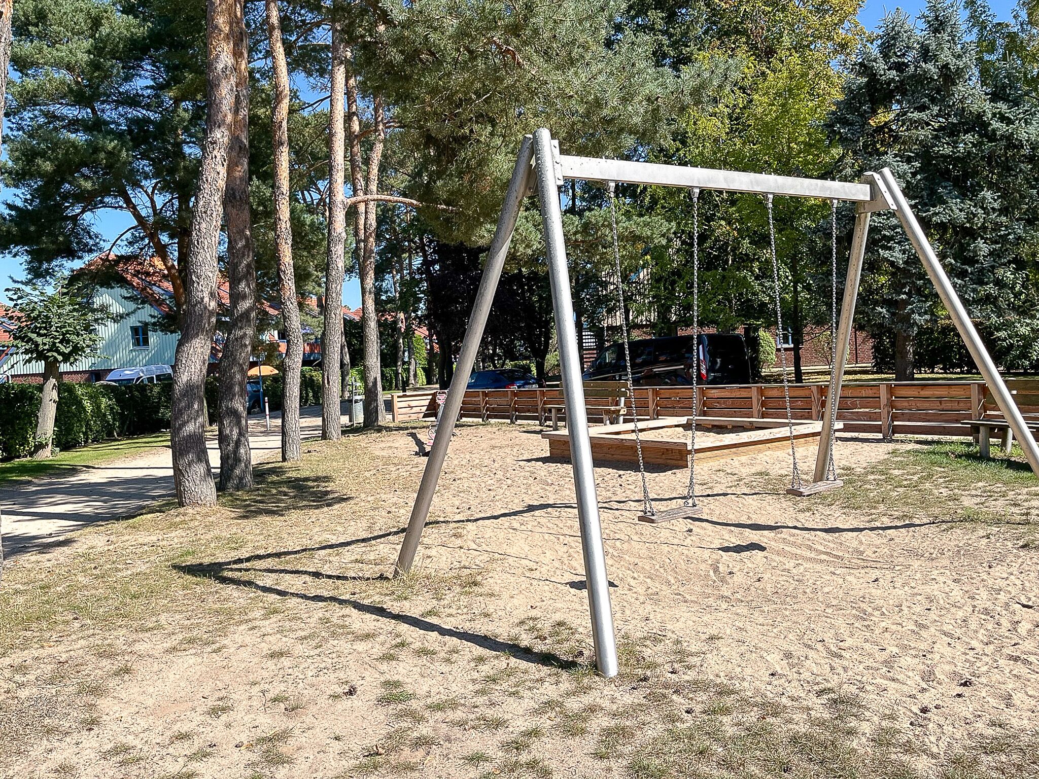 A playground with swings and benches, surrounded by trees and a building in the background.