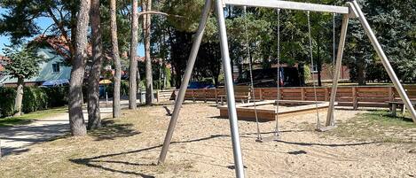 A playground with swings and benches, surrounded by trees and a building in the background.