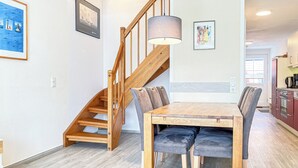 Ein Essbereich mit Holztisch und Stühlen, eine Treppe und eine Küche im Hintergrund.