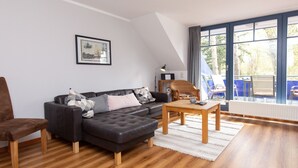 Een moderne woonkamer met een donker leren bank, een houten salontafel en een groot raam met uitzicht op de omgeving.