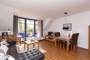 Un salon moderne comprenant un canapé, une table à manger et des chaises, de grandes fenêtres et un téléviseur.