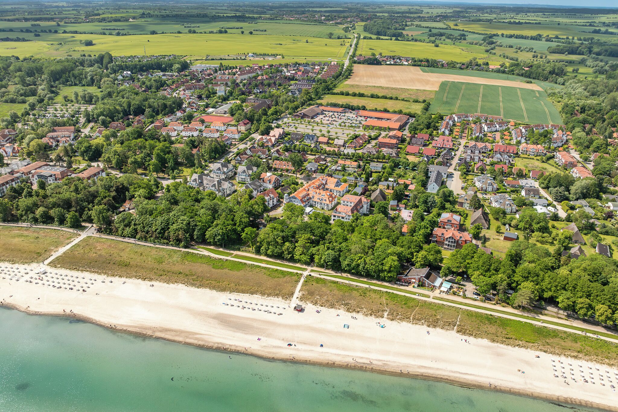 An aerial view of a coastal town with a beach, residential areas, and agricultural fields.