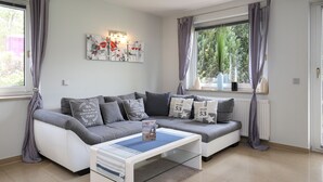 A modern living room with a grey sofa, a glass coffee table, and a large window with curtains. - Urlauberdorf Haus 63a (Ostseebad Boltenhagen)