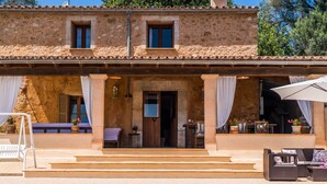 Un bâtiment en pierre avec une piscine devant, doté d’une entrée couverte, d’un espace de repos extérieur et d’un escalier menant à l’entrée.