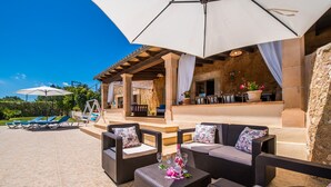 Un espace extérieur aménagé avec des meubles en osier, une table avec une bouteille et des parasols.
