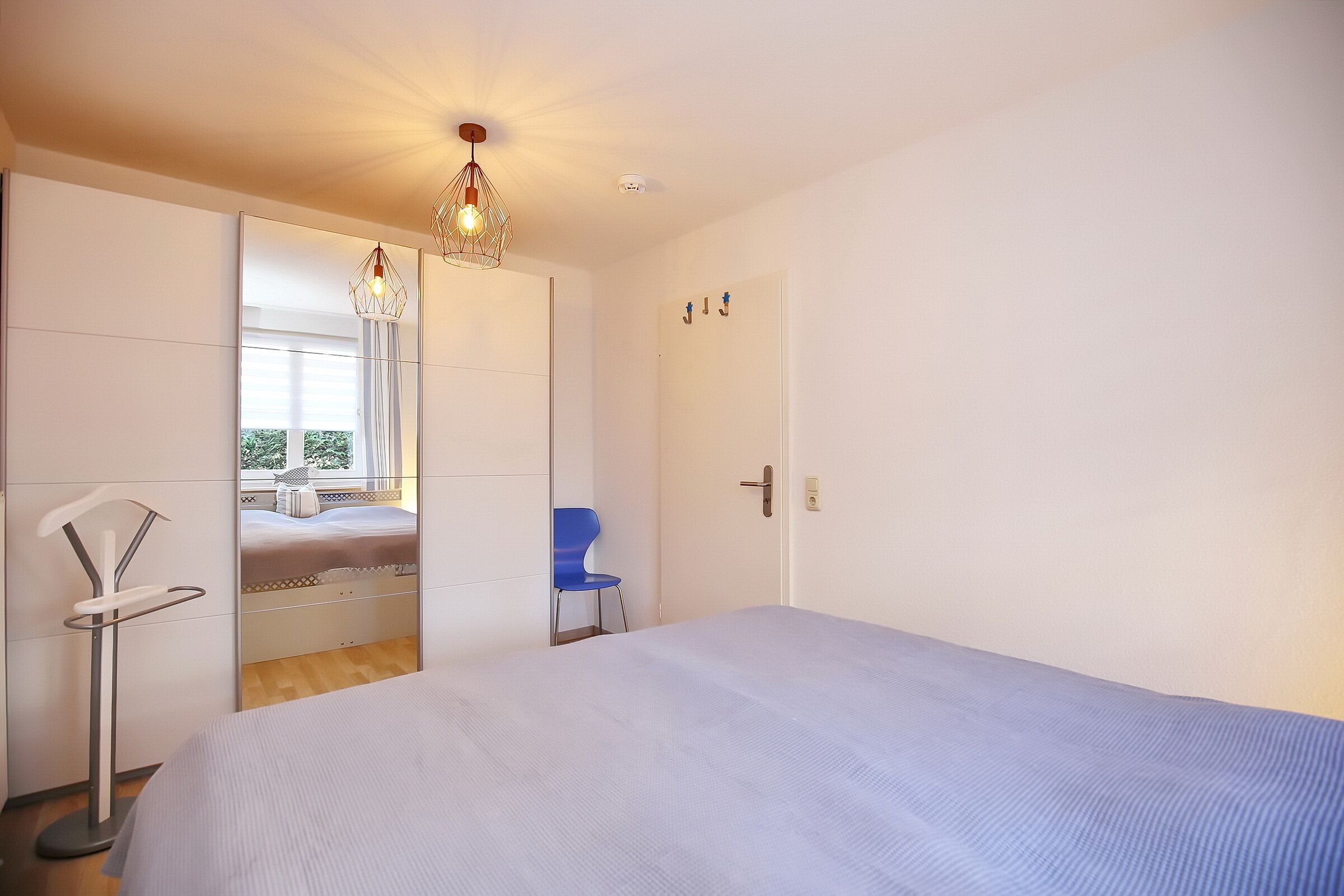 A bedroom with a bed, a chair, a wardrobe, and a hanging light fixture.