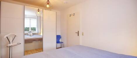 A bedroom with a bed, a chair, a wardrobe, and a hanging light fixture.