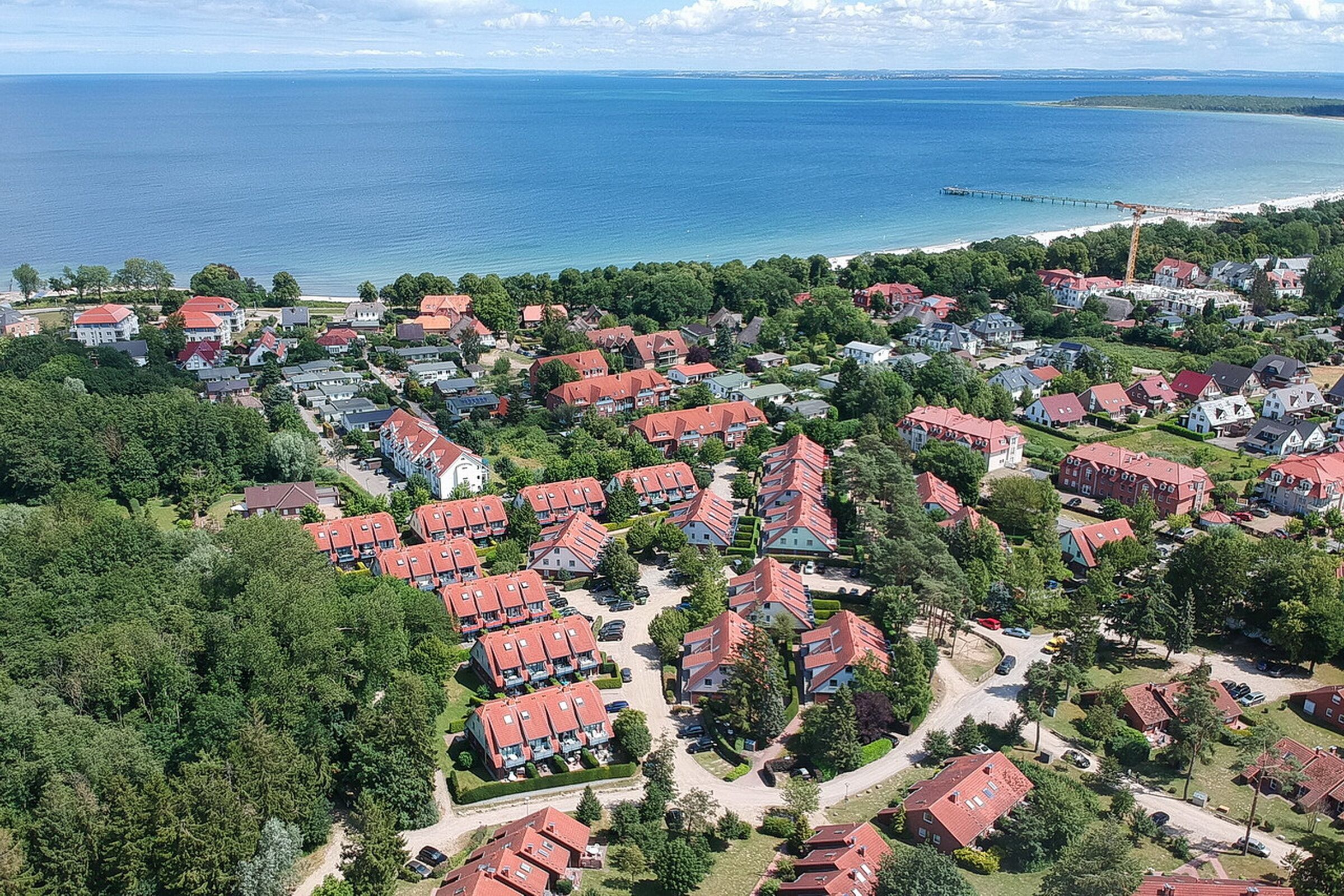 An aerial view of a coastal residential area with houses, roads, and a pier extending into the water.