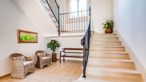 A staircase with a wooden handrail, a potted plant, and wicker furniture in a well-lit room with tiled flooring. - Country house in Mallorca Cas Cuni with pool (Felanitx)