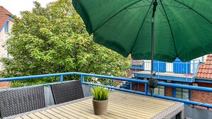 Ein Balkon mit Tisch, Stühlen und einem grünen Sonnenschirm.