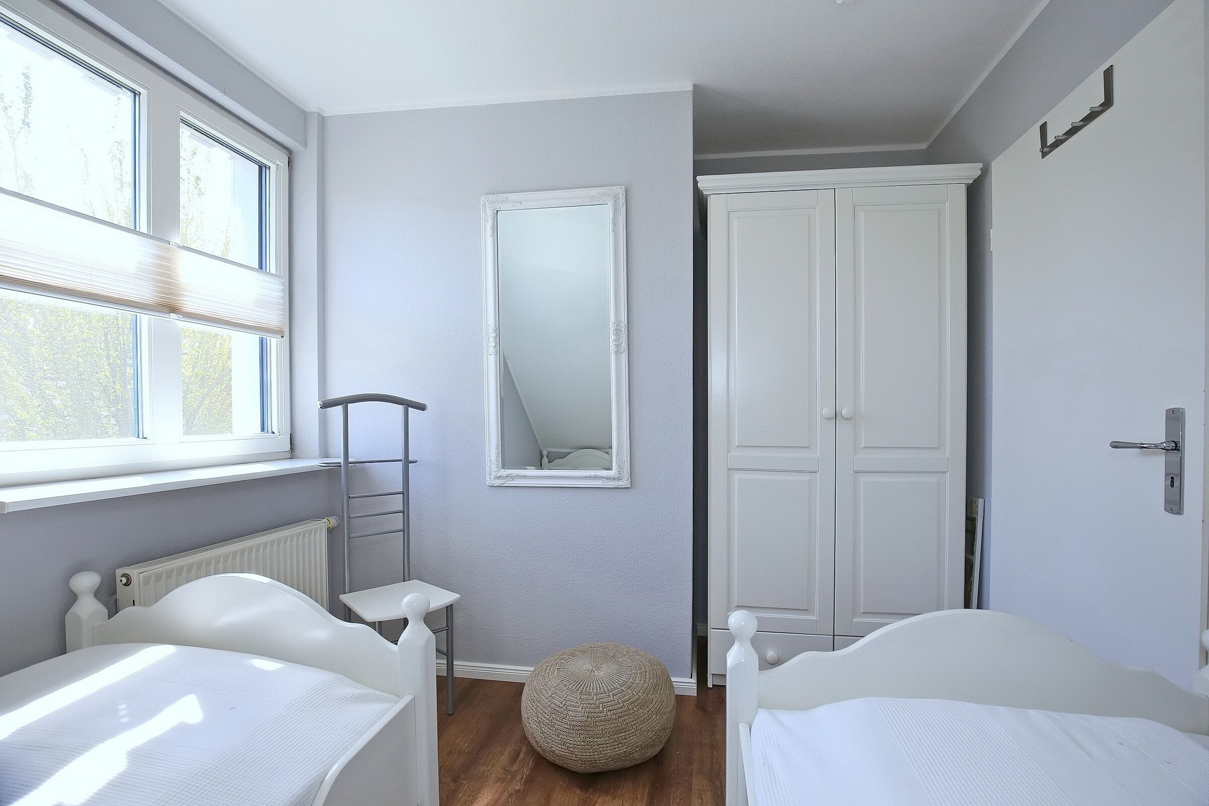 Een slaapkamer met twee bedden, een grote spiegel, een kast en een radiator.