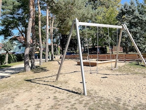 A playground with swings and benches, surrounded by trees and a building in the background.
