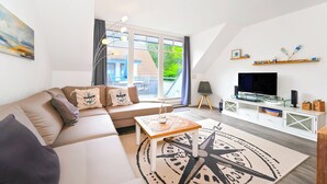 Een moderne woonkamer met een bank, salontafel, televisie en een groot raam.