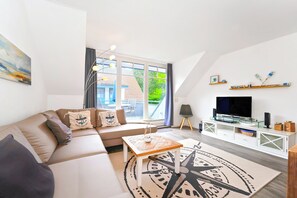 A modern living room with a sofa, coffee table, TV, and a large window. - Papillon Wohnung 04-6 (Ostseebad Boltenhagen)