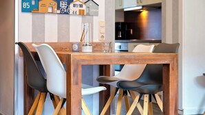 Een eetgedeelte met een houten tafel en stoelen, een keuken op de achtergrond, en een muur met decoraties in de vorm van huisjes.