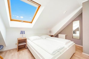 A bedroom with a skylight, a bed, a nightstand with a lamp, a radiator, and a mirror. - Papillon Wohnung 04-6 (Ostseebad Boltenhagen)