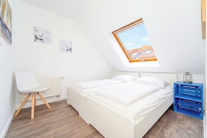 A bedroom with a skylight, a white bed, a white chair, and a blue storage unit. - Papillon Wohnung 04-6 (Ostseebad Boltenhagen)
