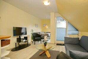 Ein modernes Wohnzimmer mit einem Flachbildfernseher, einem Glastisch, einer Couch und einem Essbereich mit Tisch und Stühlen.