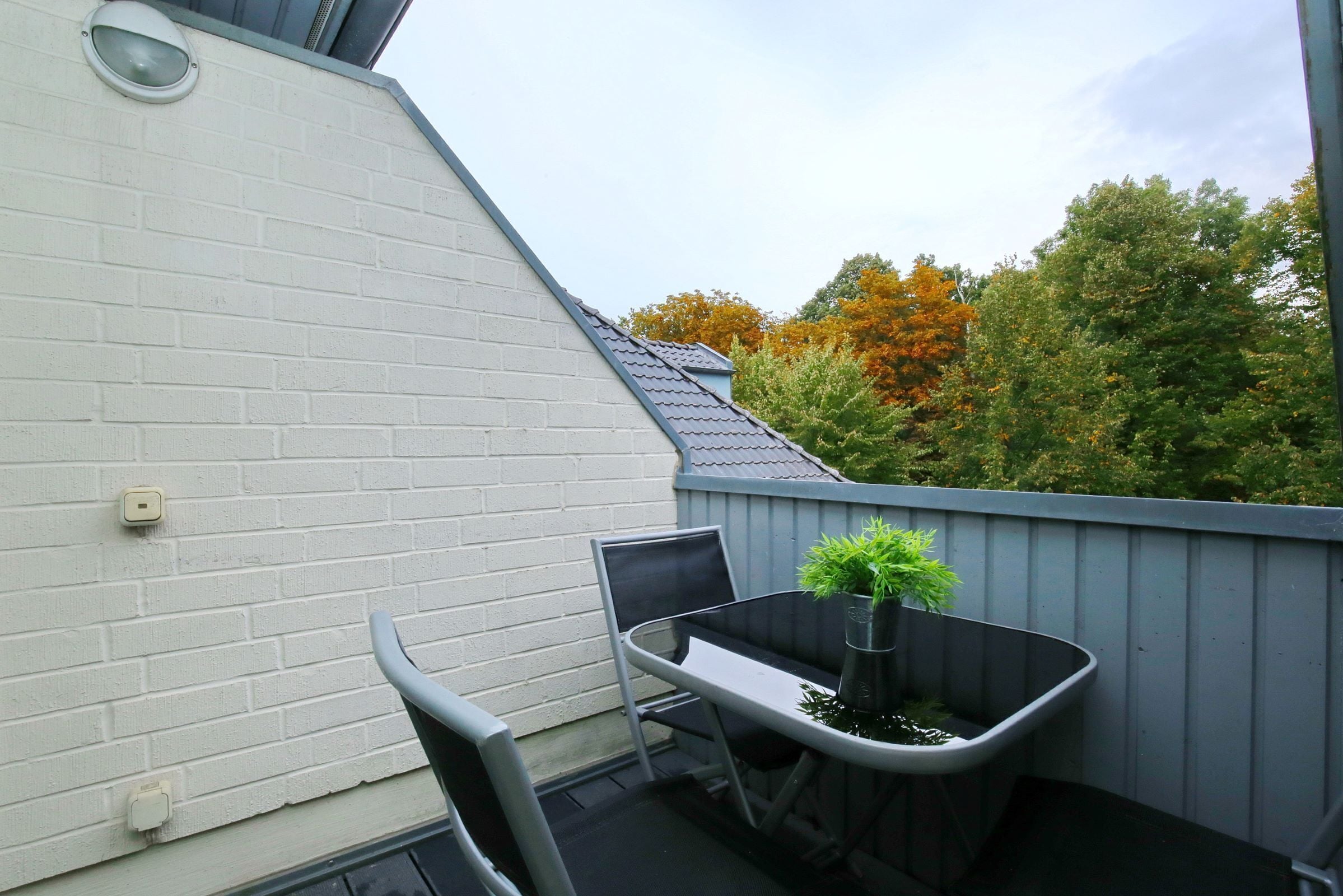 A balcony with a white brick wall, a metal table, two chairs, and a potted plant.