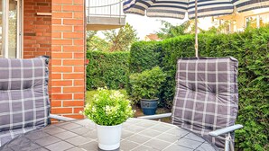 Eine Terrassengruppe im Freien mit zwei karierten Stühlen, einem Blumentopf und einem gestreiften Sonnenschirm.