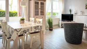 Ein Essbereich mit Tisch für vier Personen, einem Schrank mit Glastüren, einem Fernseher und einem großen gewebten Pouf.