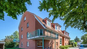 Un bâtiment en briques rouges avec un balcon, des vélos garés à l’extérieur et une voiture dans l’allée.