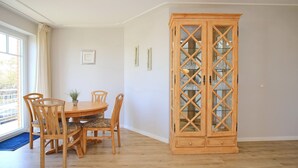 Un coin repas avec une table et des chaises en bois, un meuble avec des portes en verre et une vue par la fenêtre.