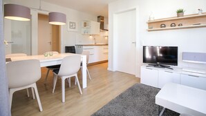 Een moderne keuken met witte kasten, een eethoek met een witte tafel en stoelen, en een televisie op een witte kast.