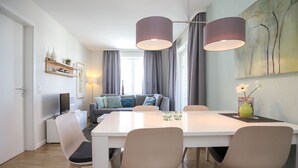 Een moderne eetruimte met een witte tafel en stoelen, een groot schilderij aan de muur en een bank op de achtergrond.