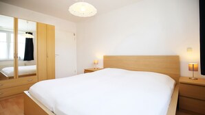 Un dormitorio con una cama grande, un armario de madera, lámparas de noche y una lámpara en el techo.