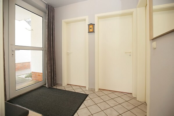 Un pasillo con puerta corredera de vidrio que da a un área exterior, un felpudo negro en la entrada y piso de baldosas.